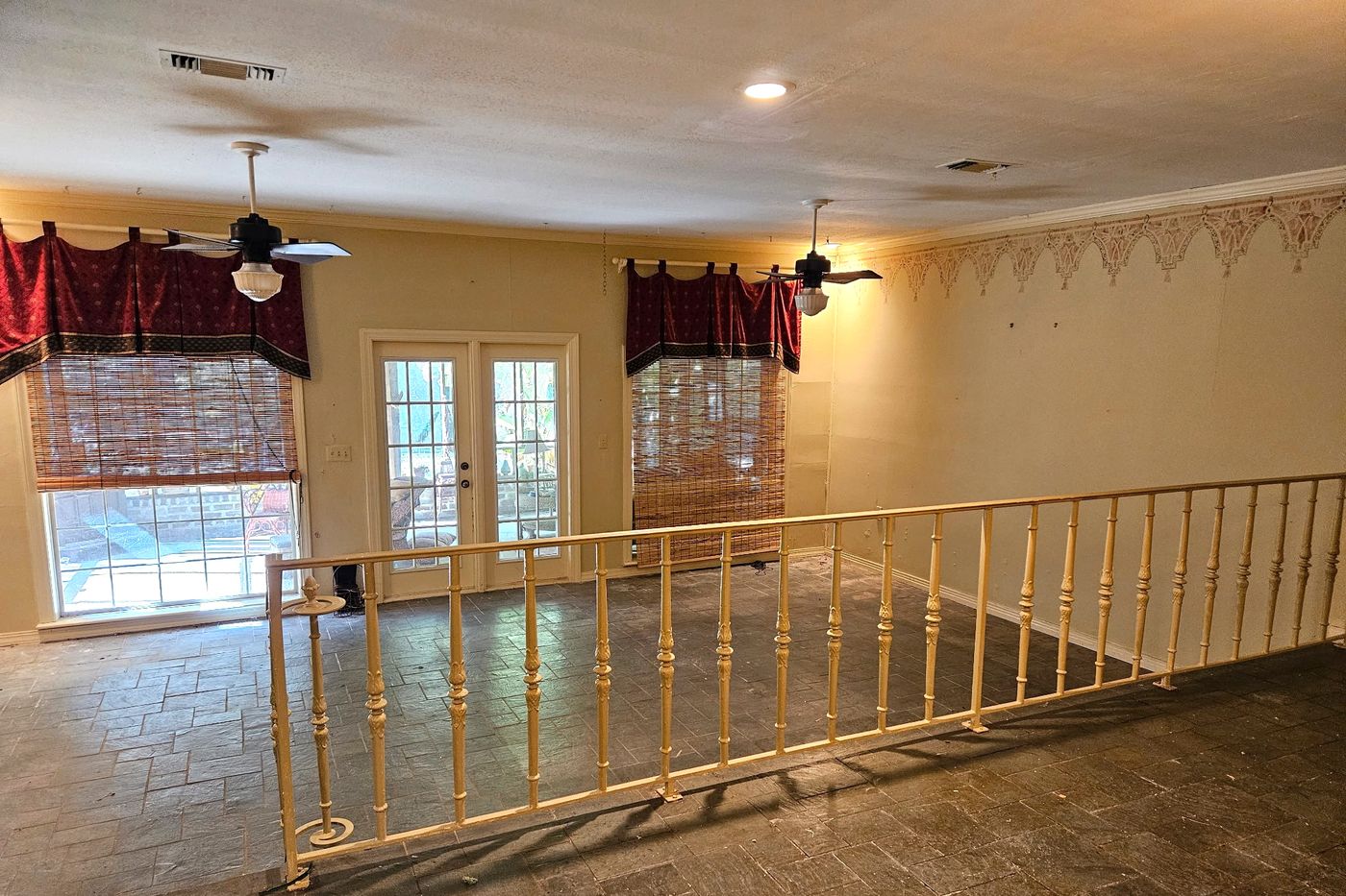 Long room with a dark tile floor, a turned-spindle railing across the space, two ceiling fans, and French doors between two windows on the far wall